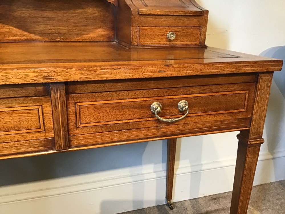 An antique mahogany writing desk featuring a central leather surface, a raised superstructure with stationery compartments, two frieze drawers, and tapered legs on brass castors. View VIII