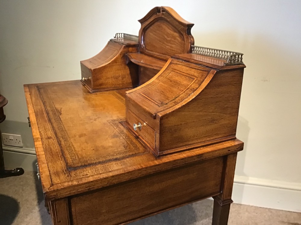 An antique mahogany writing desk featuring a central leather surface, a raised superstructure with stationery compartments, two frieze drawers, and tapered legs on brass castors. View X
