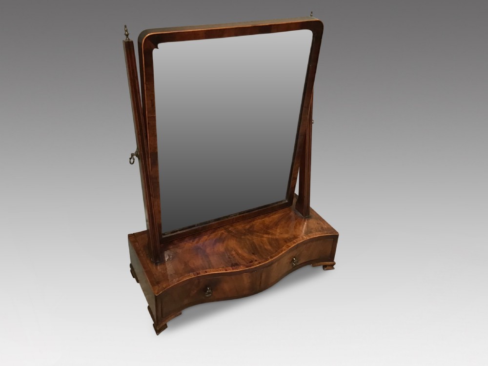 A Georgian mahogany toilet mirror featuring an adjustable glass plate set within vertical posts above a serpentine box base with drawers. View II