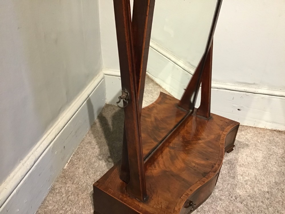 A Georgian mahogany toilet mirror featuring an adjustable glass plate set within vertical posts above a serpentine box base with drawers. View IV