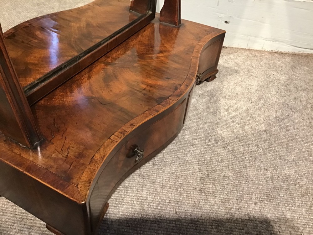 A Georgian mahogany toilet mirror featuring an adjustable glass plate set within vertical posts above a serpentine box base with drawers. View V