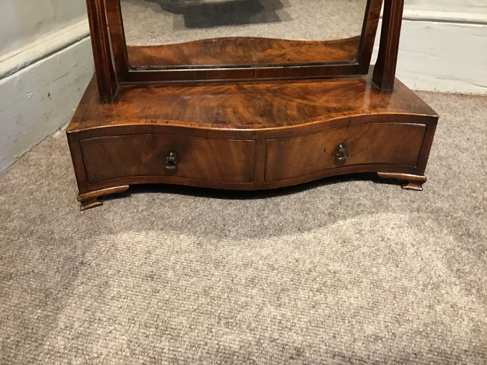 A Georgian mahogany toilet mirror featuring an adjustable glass plate set within vertical posts above a serpentine box base with drawers. View VI
