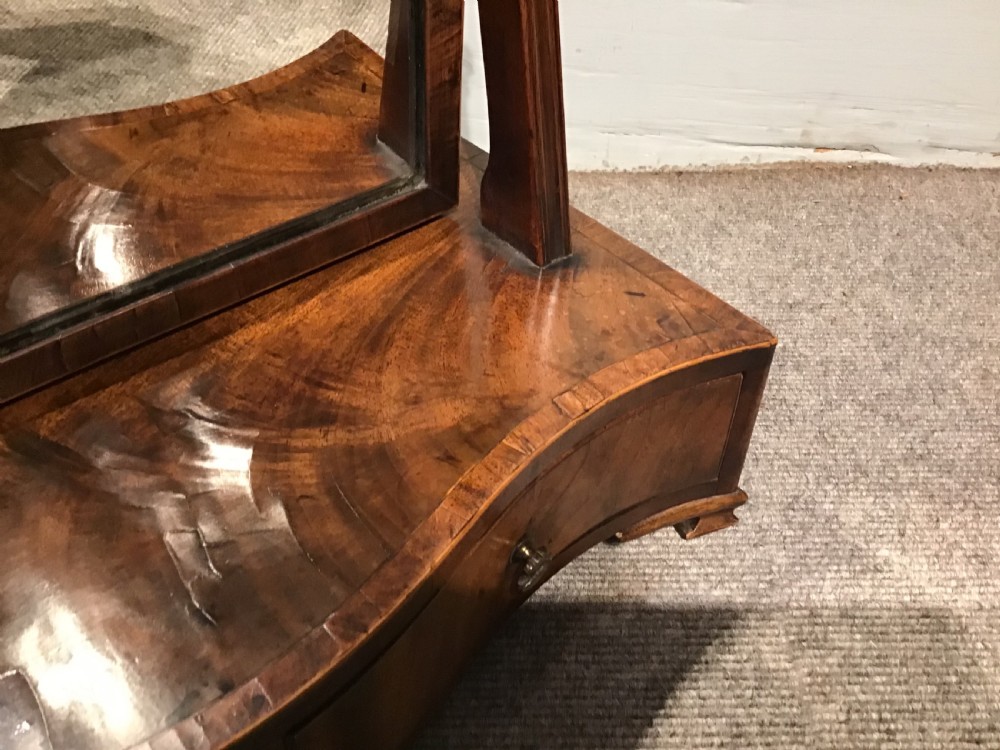 A Georgian mahogany toilet mirror featuring an adjustable glass plate set within vertical posts above a serpentine box base with drawers. View IX