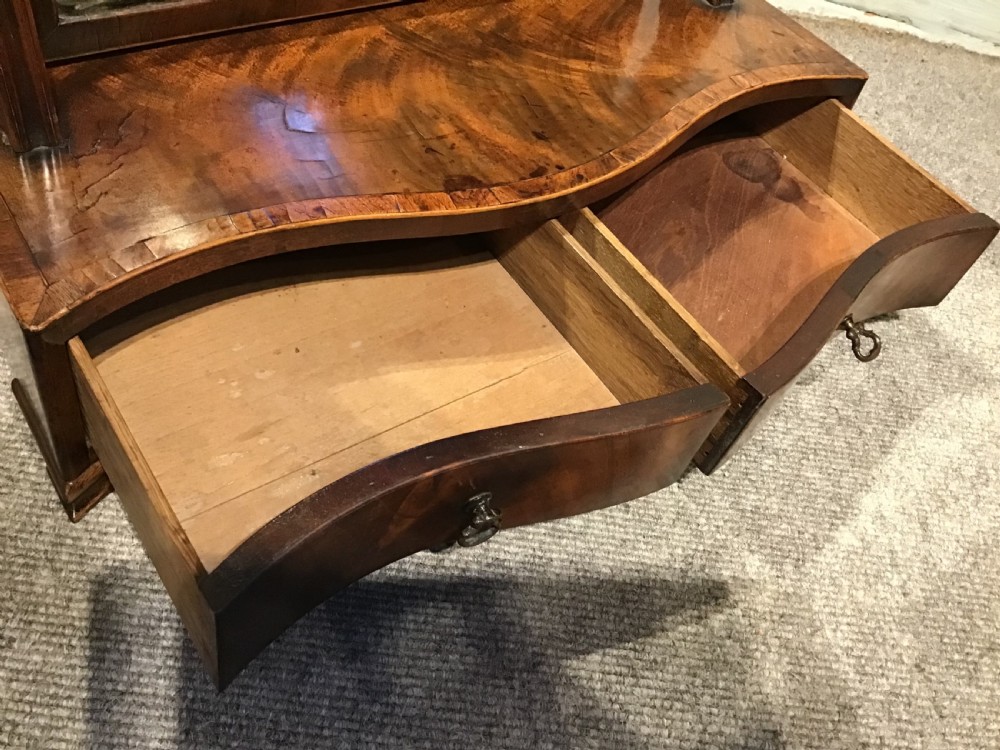 A Georgian mahogany toilet mirror featuring an adjustable glass plate set within vertical posts above a serpentine box base with drawers. View X