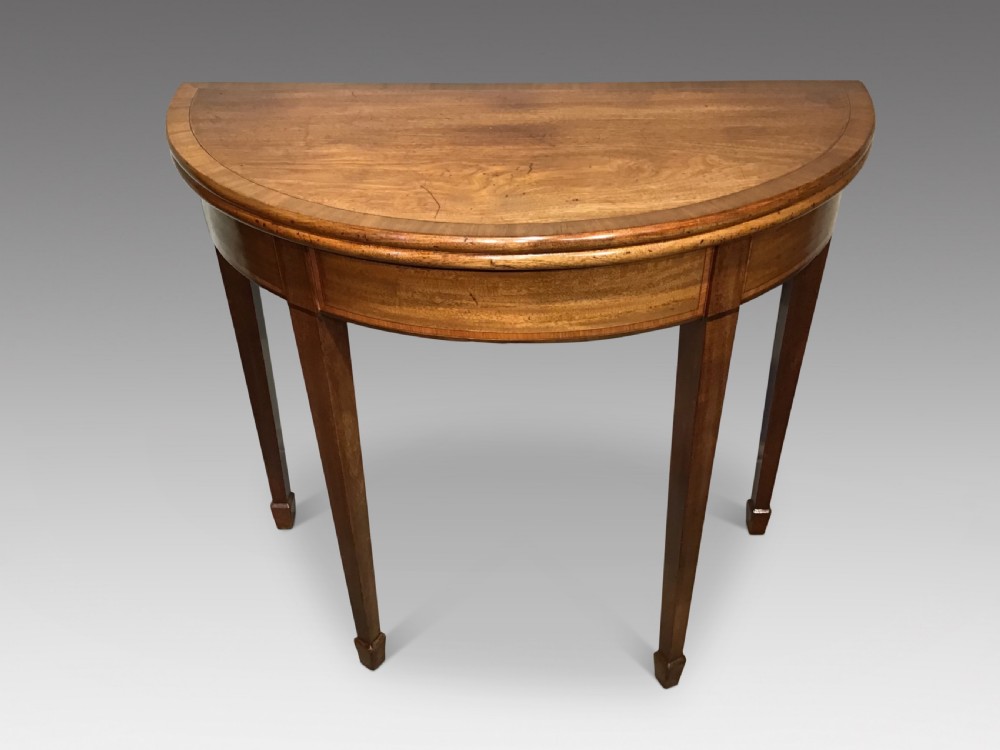 A semi-circular antique mahogany demi-lune table with inlaid apron borders and four tapered square legs.