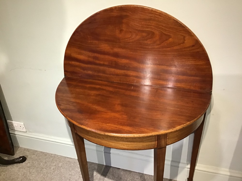 A semi-circular antique mahogany demi-lune table with inlaid apron borders and four tapered square legs. View VI