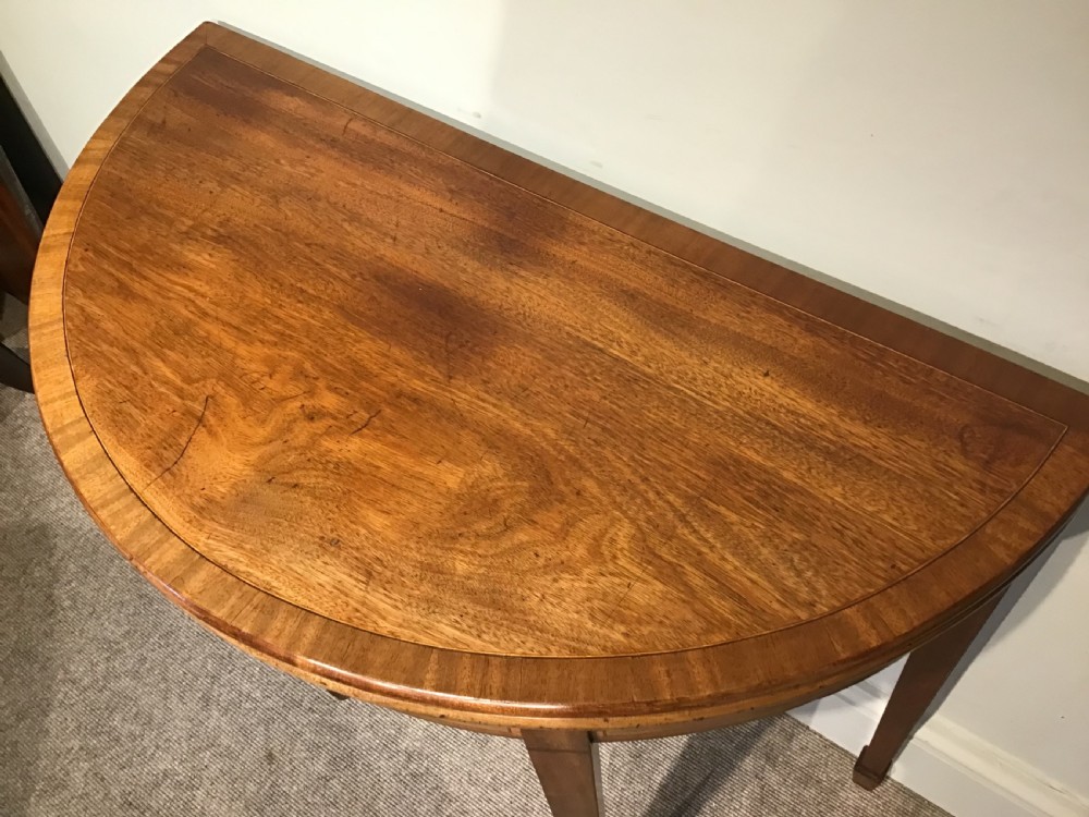 A semi-circular antique mahogany demi-lune table with inlaid apron borders and four tapered square legs. View VII