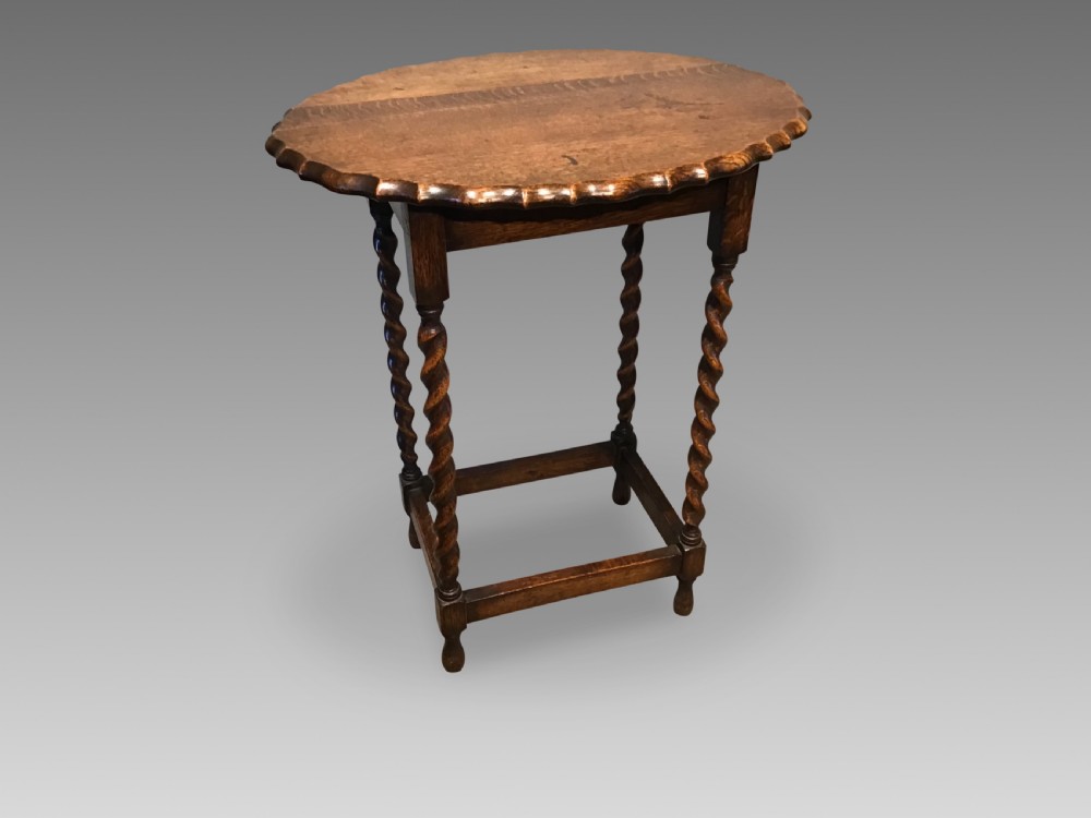 An antique oak occasional table featuring a scalloped piecrust oval top, four spiral barley twist legs, and a lower box stretcher.