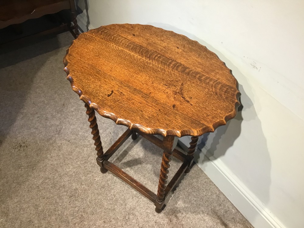 An antique oak occasional table featuring a scalloped piecrust oval top, four spiral barley twist legs, and a lower box stretcher. View II