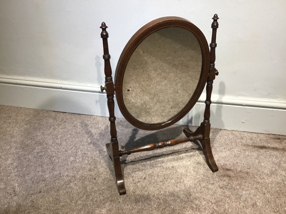 An antique oval toilet mirror crafted from dark polished wood with turned side supports and a stretcher base.