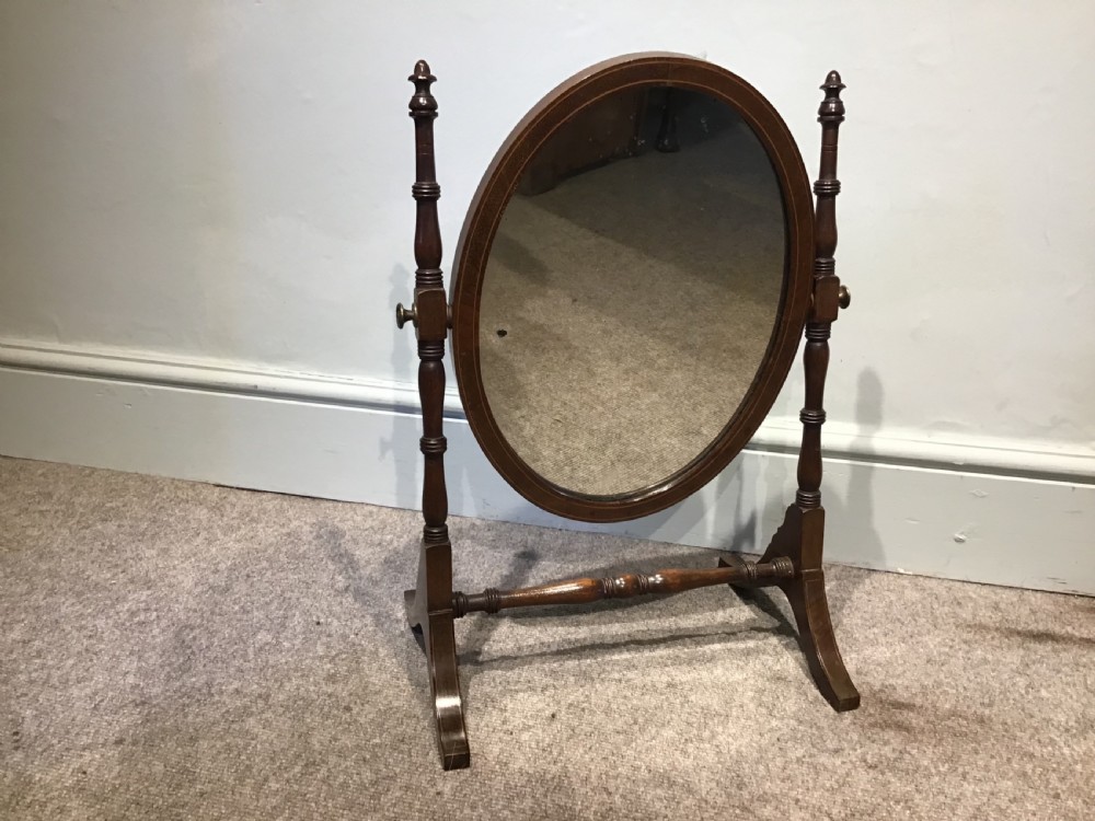 An antique oval toilet mirror crafted from dark polished wood with turned side supports and a stretcher base. View II