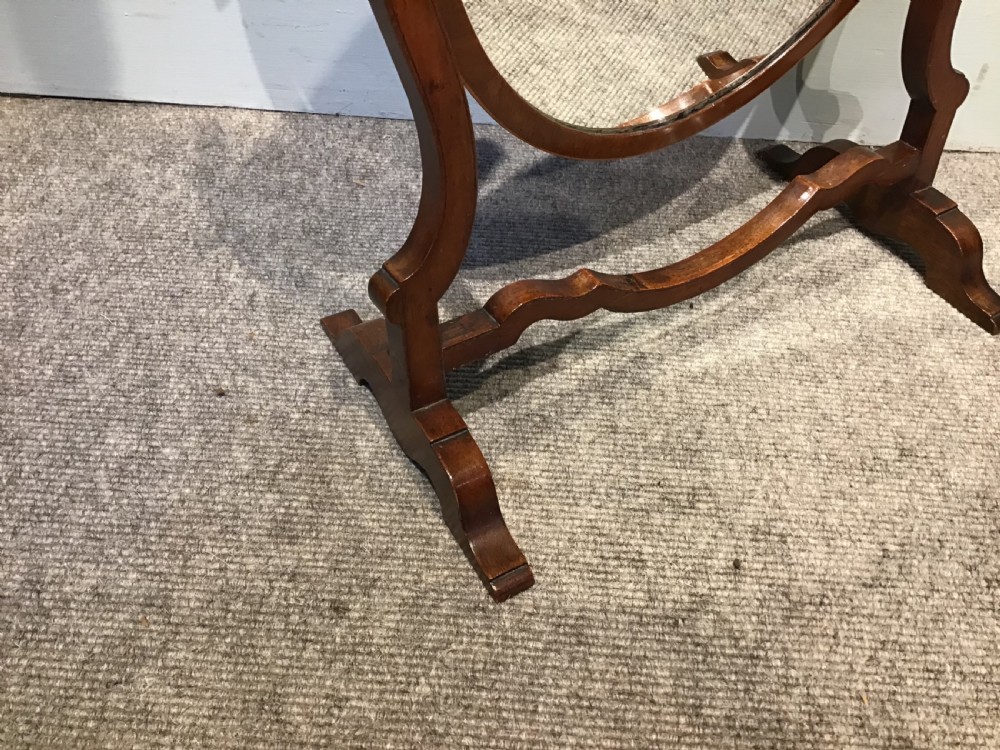 An antique oval mahogany swing mirror featuring curved upright supports and a shaped stretcher base. View II
