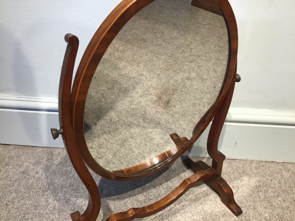 An antique oval mahogany swing mirror featuring curved upright supports and a shaped stretcher base. View III