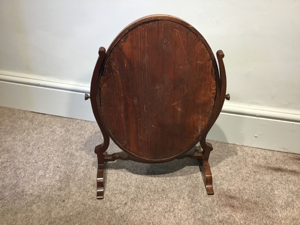 An antique oval mahogany swing mirror featuring curved upright supports and a shaped stretcher base. View IV