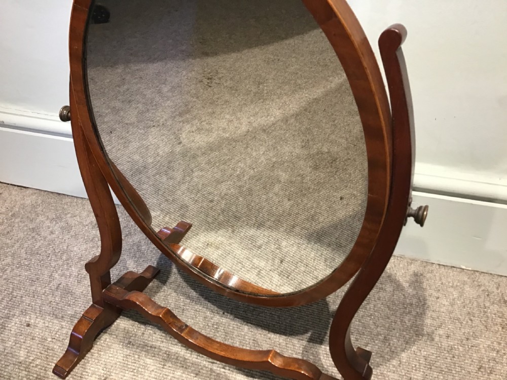 An antique oval mahogany swing mirror featuring curved upright supports and a shaped stretcher base. View V