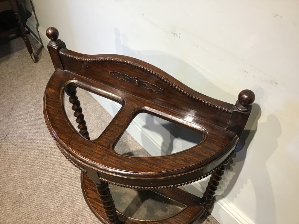 An antique dark oak demilune stick stand featuring three barley twist legs, beaded carved details, two top sections, ball finials, and a fitted metal drip tray. View II