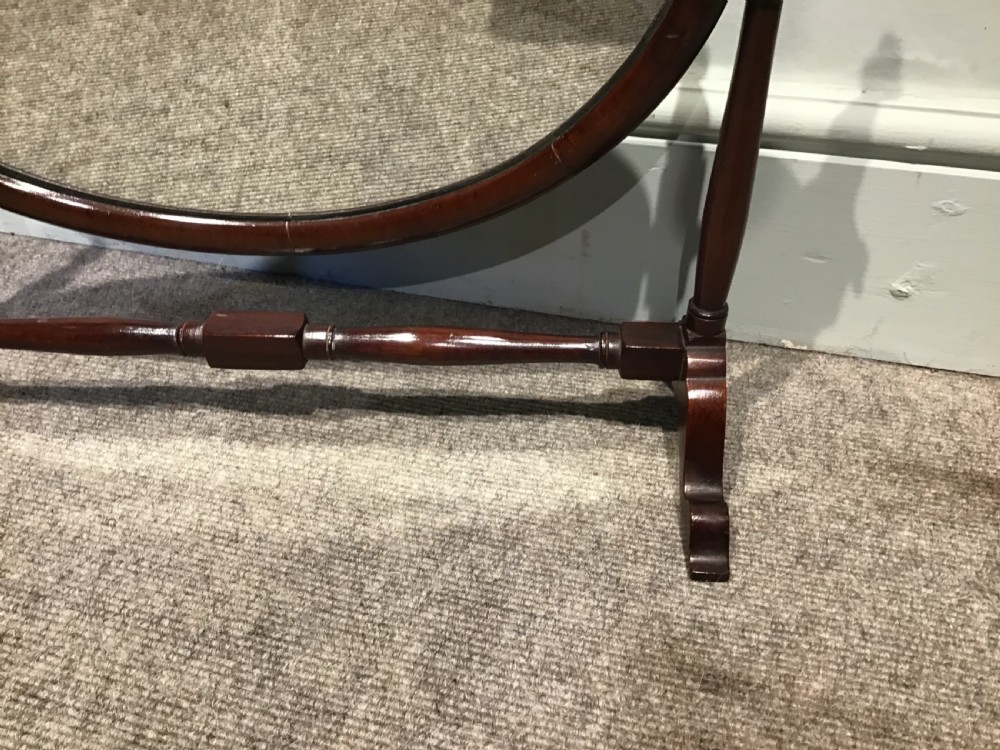 An antique oval mahogany skeleton mirror featuring turned side posts with finials and a swivel mechanism on a low wooden base. View II