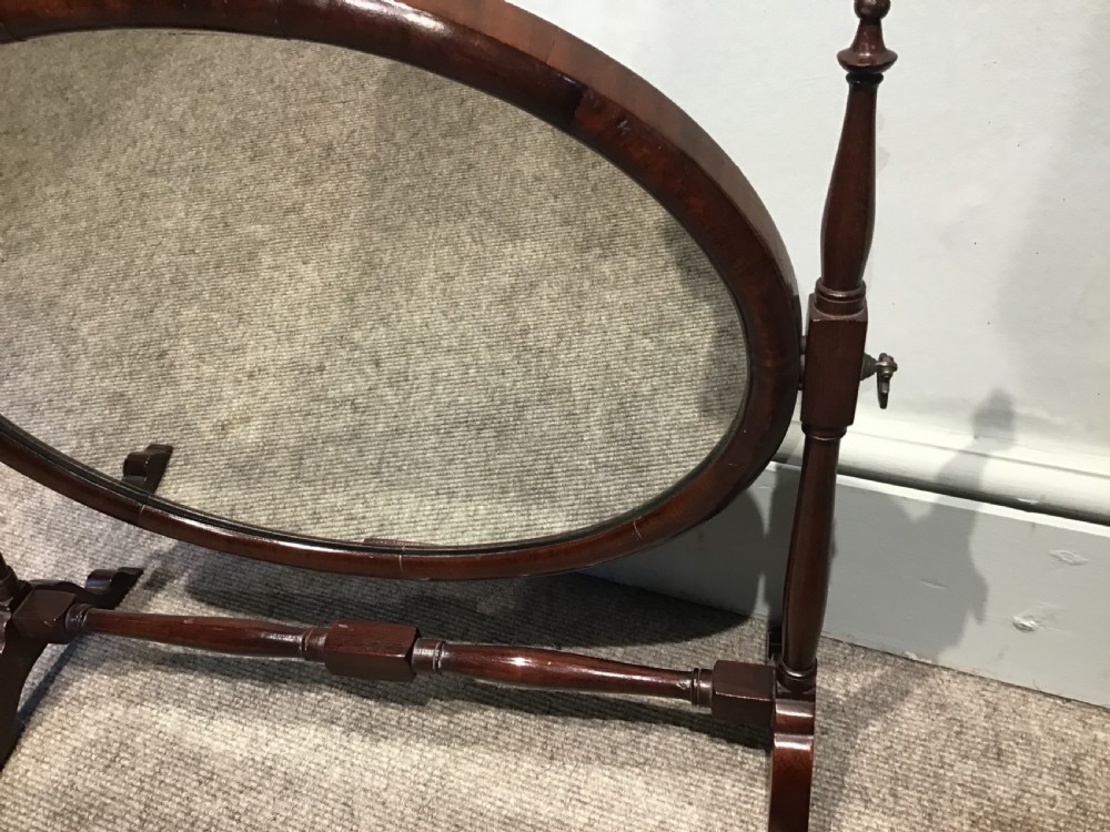 An antique oval mahogany skeleton mirror featuring turned side posts with finials and a swivel mechanism on a low wooden base. View III
