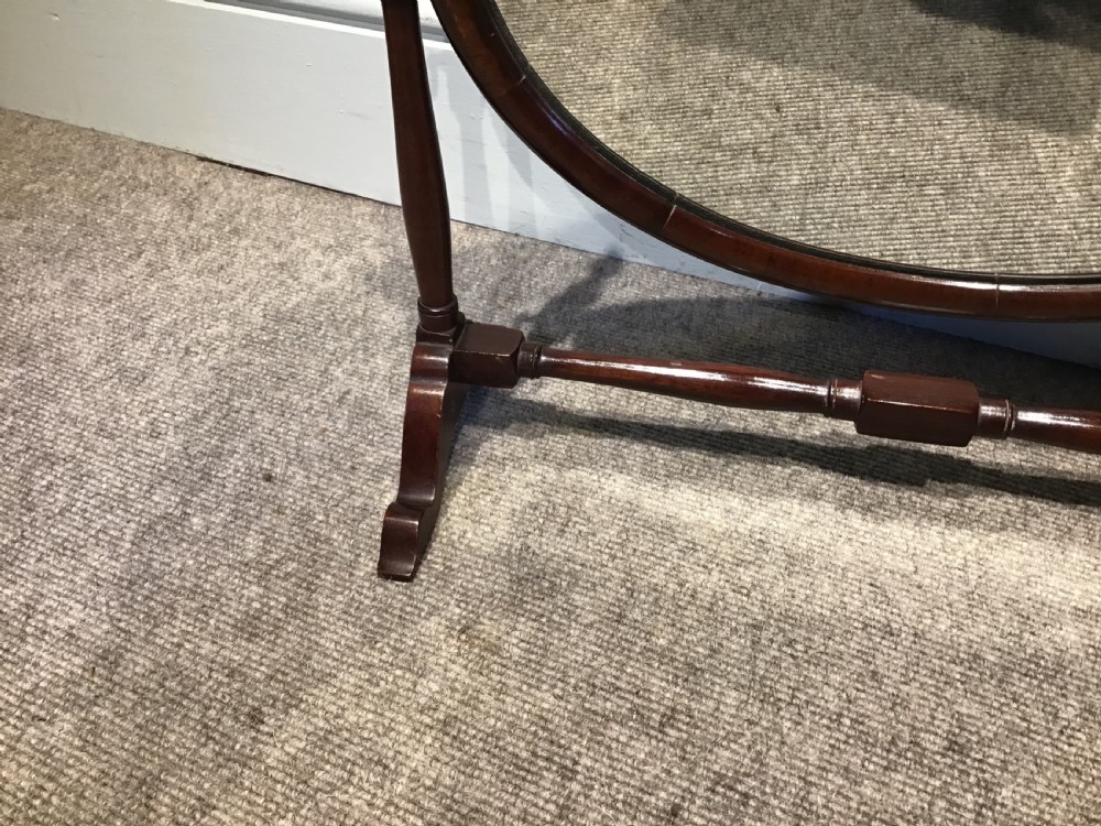 An antique oval mahogany skeleton mirror featuring turned side posts with finials and a swivel mechanism on a low wooden base. View IV