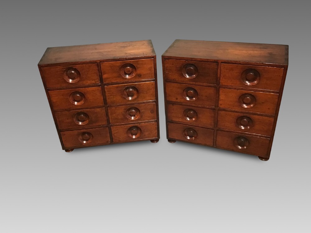 A pair of antique brown wooden apothecary chests, each featuring eight drawers with carved circular recessed handles.