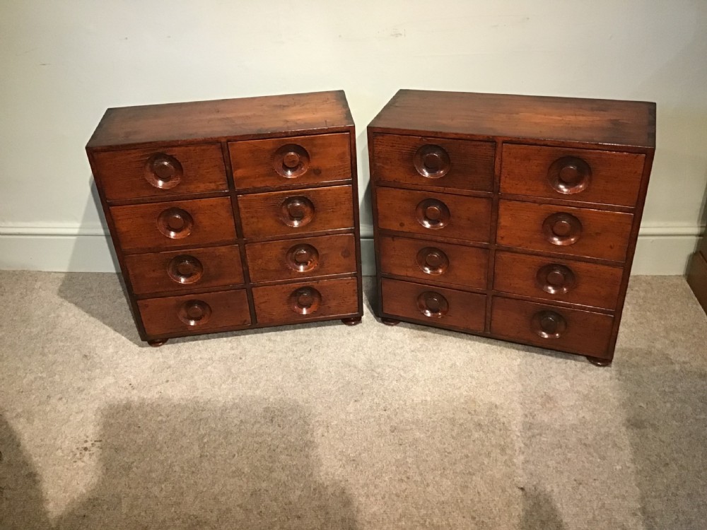 A pair of antique brown wooden apothecary chests, each featuring eight drawers with carved circular recessed handles. View II