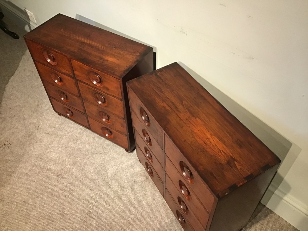 A pair of antique brown wooden apothecary chests, each featuring eight drawers with carved circular recessed handles. View III