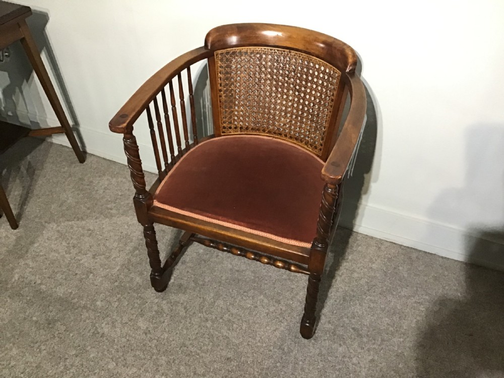 An antique mahogany tub chair featuring a woven cane back panel, turned side spindles, barley twist legs, and a dark brown upholstered seat. View II