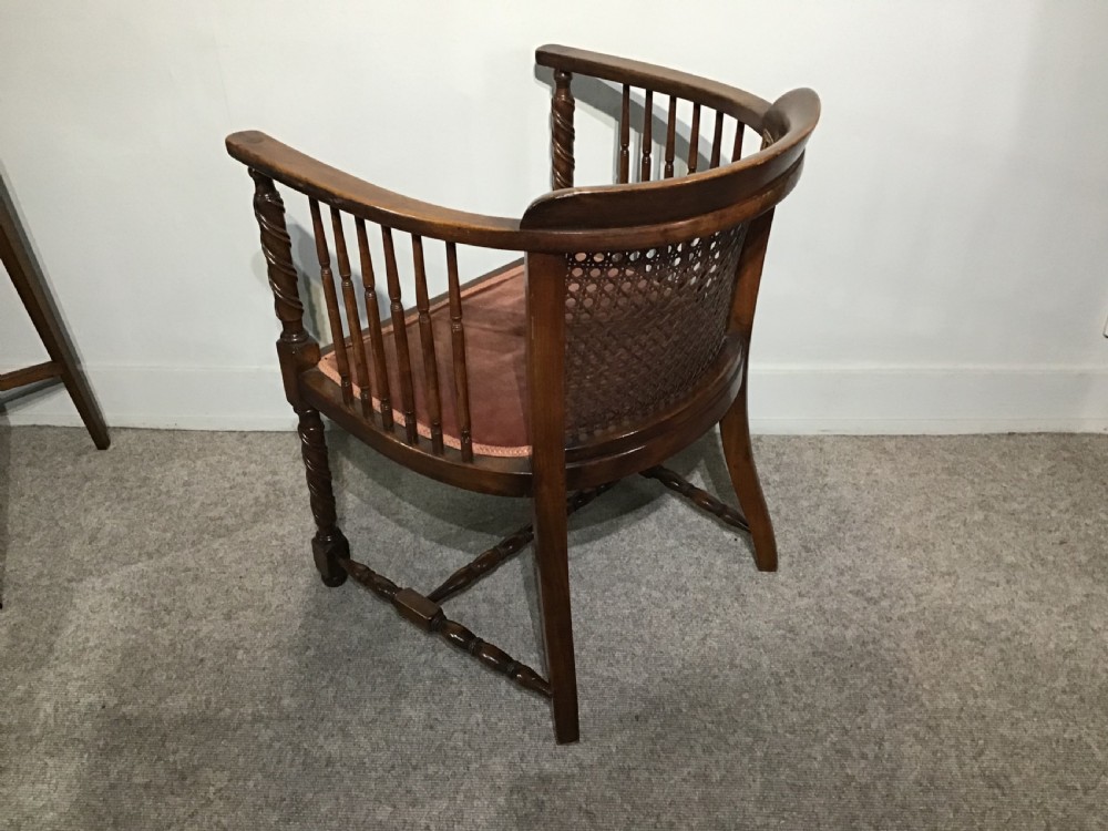 An antique mahogany tub chair featuring a woven cane back panel, turned side spindles, barley twist legs, and a dark brown upholstered seat. View VII