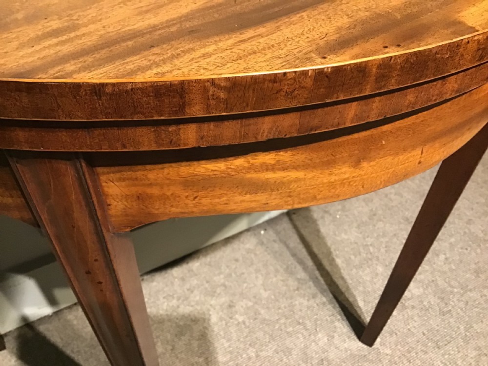 A semi-circular antique mahogany demi-lune card table featuring four square tapered legs and a patterned flame mahogany veneered top surface. View VI