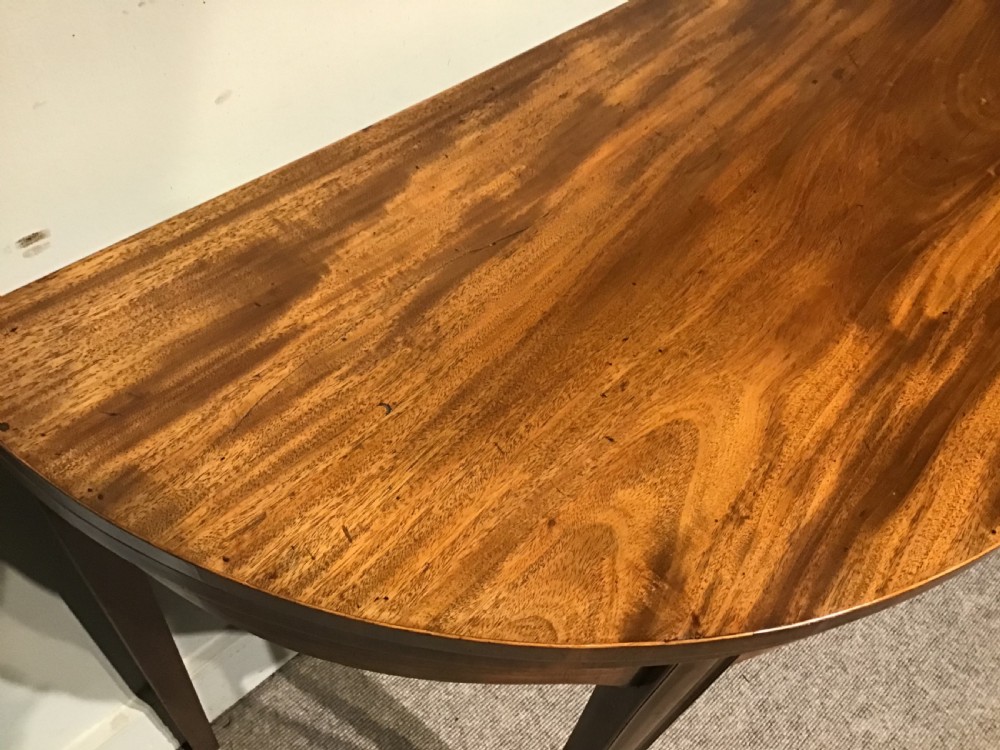 A semi-circular antique mahogany demi-lune card table featuring four square tapered legs and a patterned flame mahogany veneered top surface. View VII