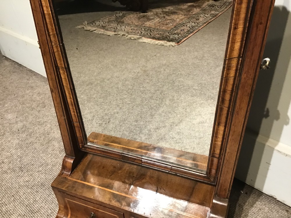 A Georgian walnut toilet mirror featuring a rectangular tilting glass frame supported by upright posts over a base with two small drawers and brass knobs. View V
