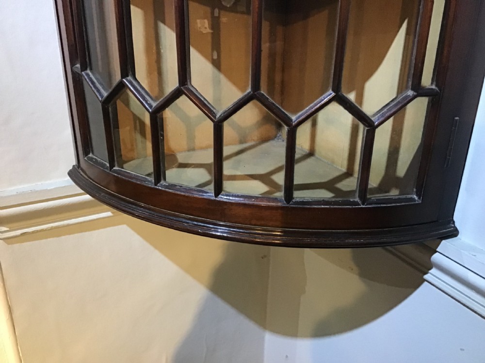 An antique Georgian bow-front mahogany corner cabinet featuring geometric astragal glazed glass doors and a carved frieze along the top cornice. View II