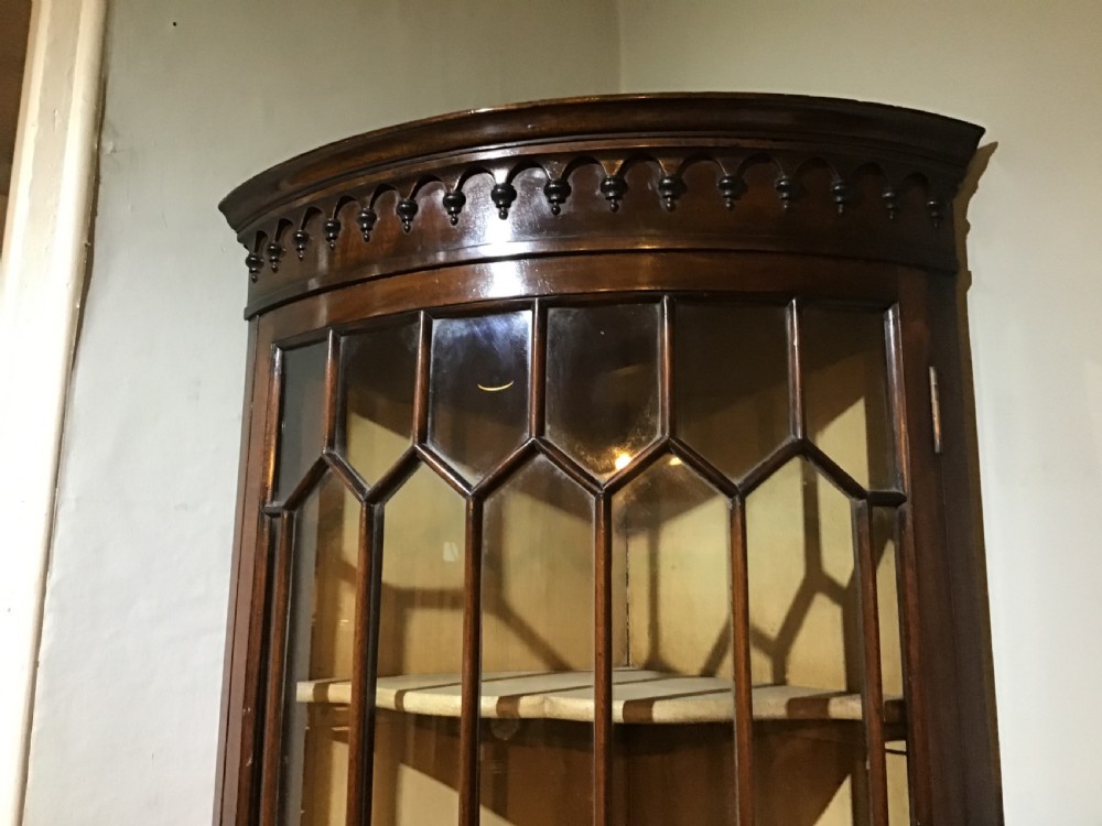 An antique Georgian bow-front mahogany corner cabinet featuring geometric astragal glazed glass doors and a carved frieze along the top cornice. View III