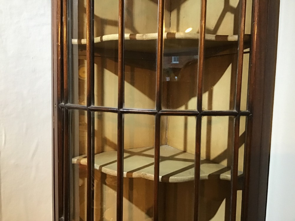 An antique Georgian bow-front mahogany corner cabinet featuring geometric astragal glazed glass doors and a carved frieze along the top cornice. View IV