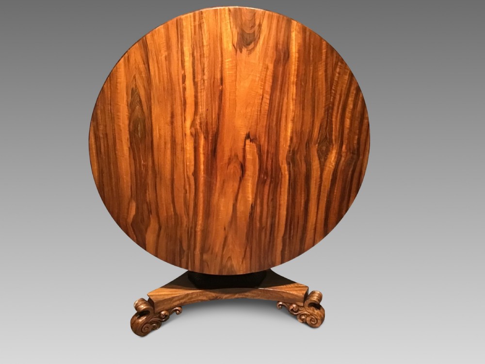 A circular William IV Goncalo Alves tilt-top centre table tilted vertically to show the figured timber grain above a triform base with carved scroll feet.