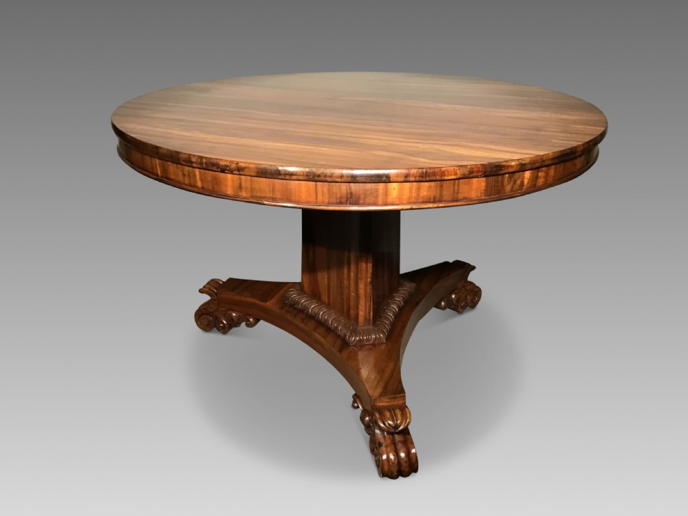 A circular William IV Goncalo Alves tilt-top centre table tilted vertically to show the figured timber grain above a triform base with carved scroll feet. View II