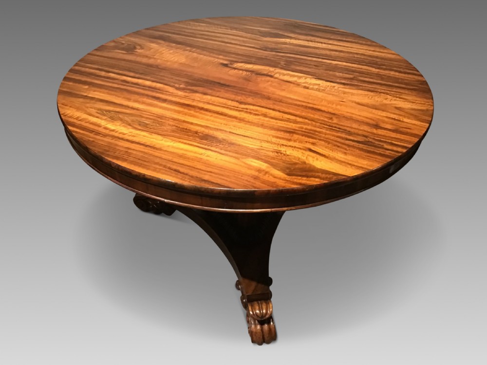 A circular William IV Goncalo Alves tilt-top centre table tilted vertically to show the figured timber grain above a triform base with carved scroll feet. View III