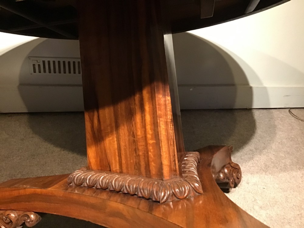 A circular William IV Goncalo Alves tilt-top centre table tilted vertically to show the figured timber grain above a triform base with carved scroll feet. View VI