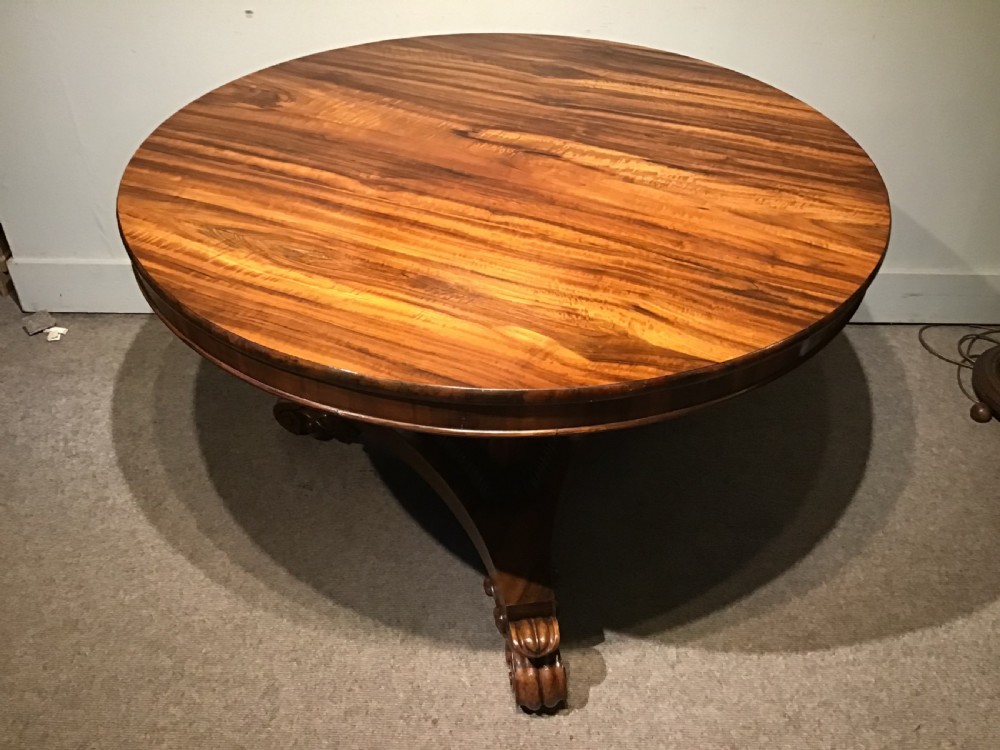 A circular William IV Goncalo Alves tilt-top centre table tilted vertically to show the figured timber grain above a triform base with carved scroll feet. View VIII