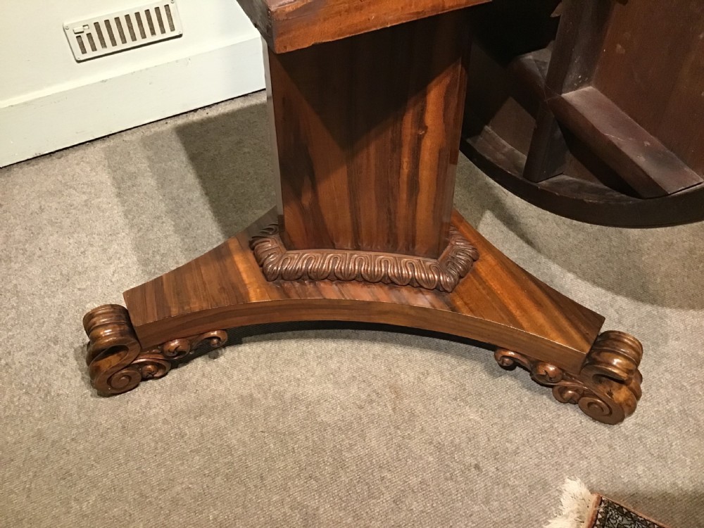 A circular William IV Goncalo Alves tilt-top centre table tilted vertically to show the figured timber grain above a triform base with carved scroll feet. View X