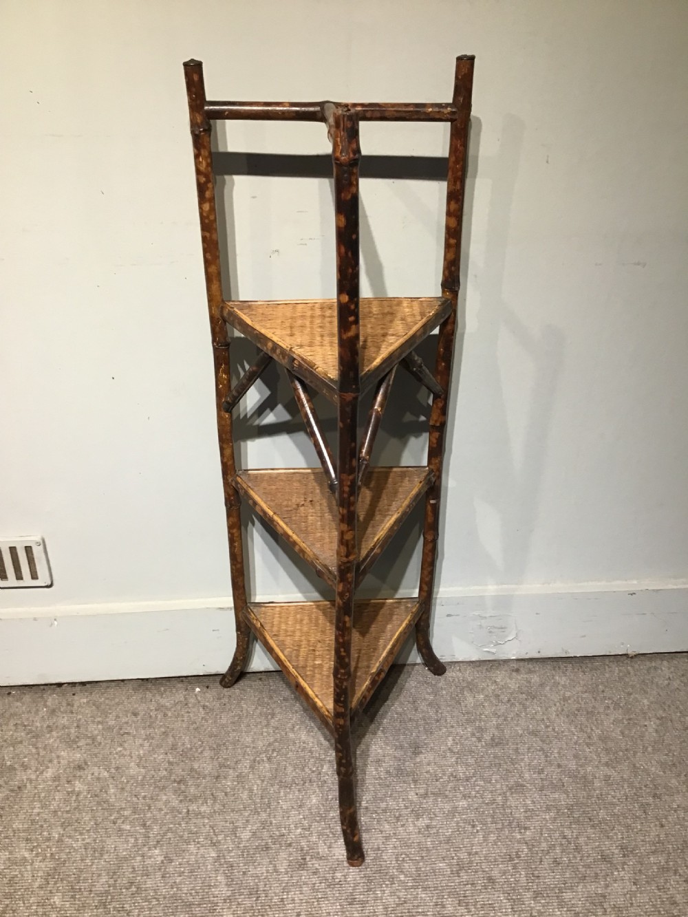 A three-tiered Victorian corner stand crafted from mottled brown bamboo with triangular woven rattan shelves.