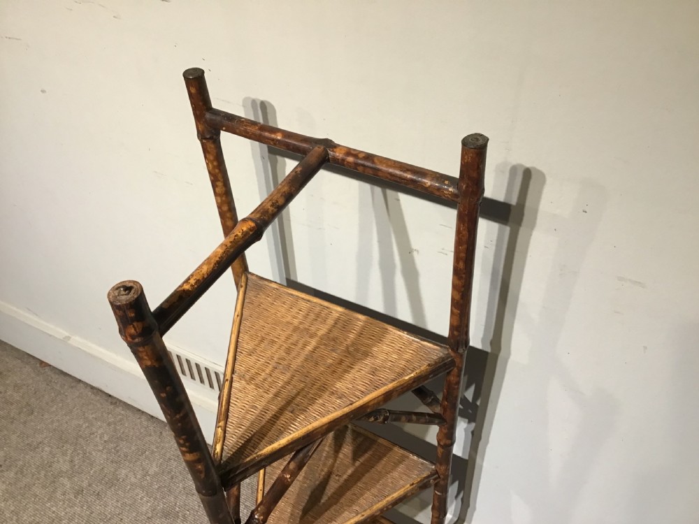 A three-tiered Victorian corner stand crafted from mottled brown bamboo with triangular woven rattan shelves. View II