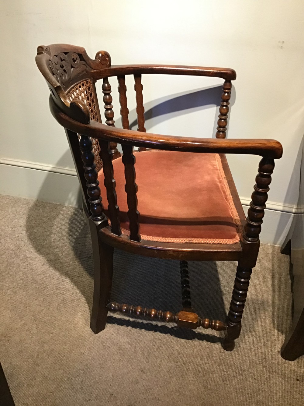 An antique dark oak tub chair featuring a carved scroll crest rail, central caned back panel, turned spindle supports, and a terracotta velvet upholstered seat. View V
