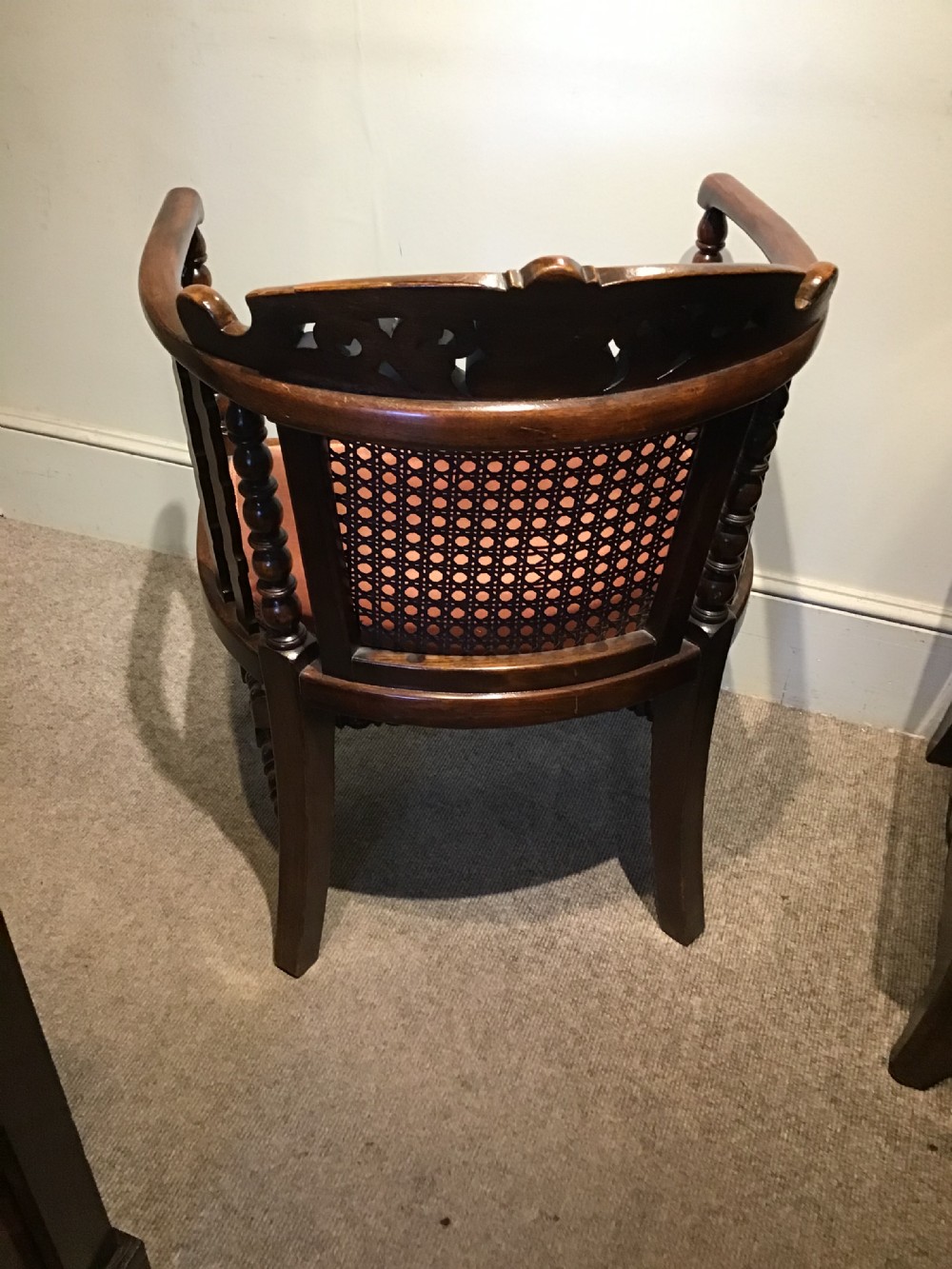 An antique dark oak tub chair featuring a carved scroll crest rail, central caned back panel, turned spindle supports, and a terracotta velvet upholstered seat. View VI