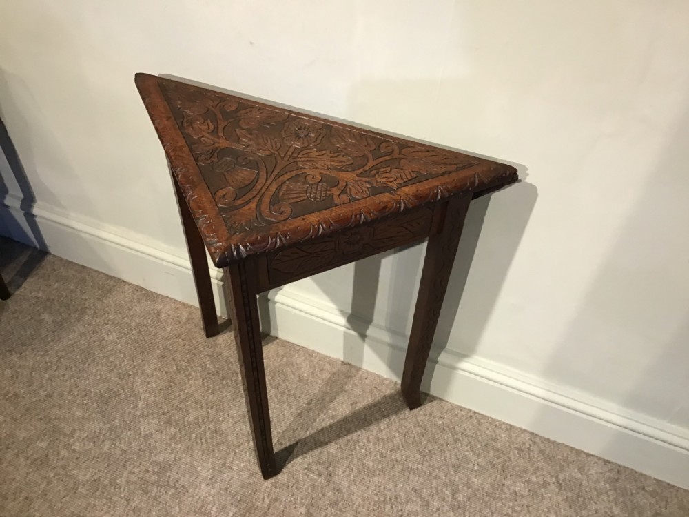 A triangular dark carved wooden corner table featuring intricate relief carvings of leaves and flowers on its top surface and legs. View II