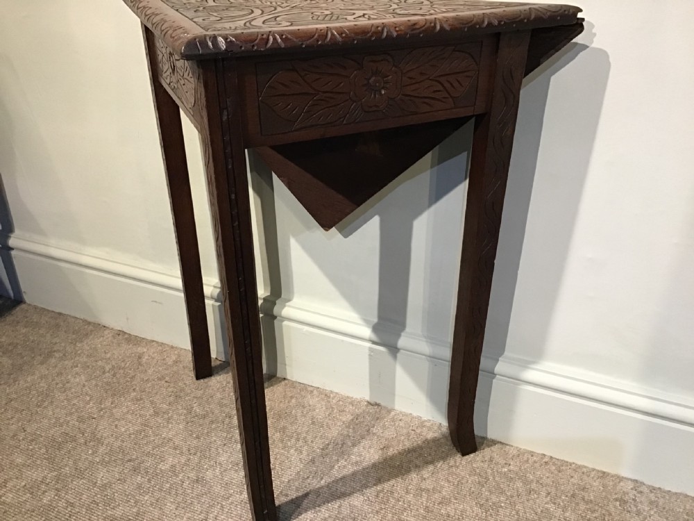 A triangular dark carved wooden corner table featuring intricate relief carvings of leaves and flowers on its top surface and legs. View III