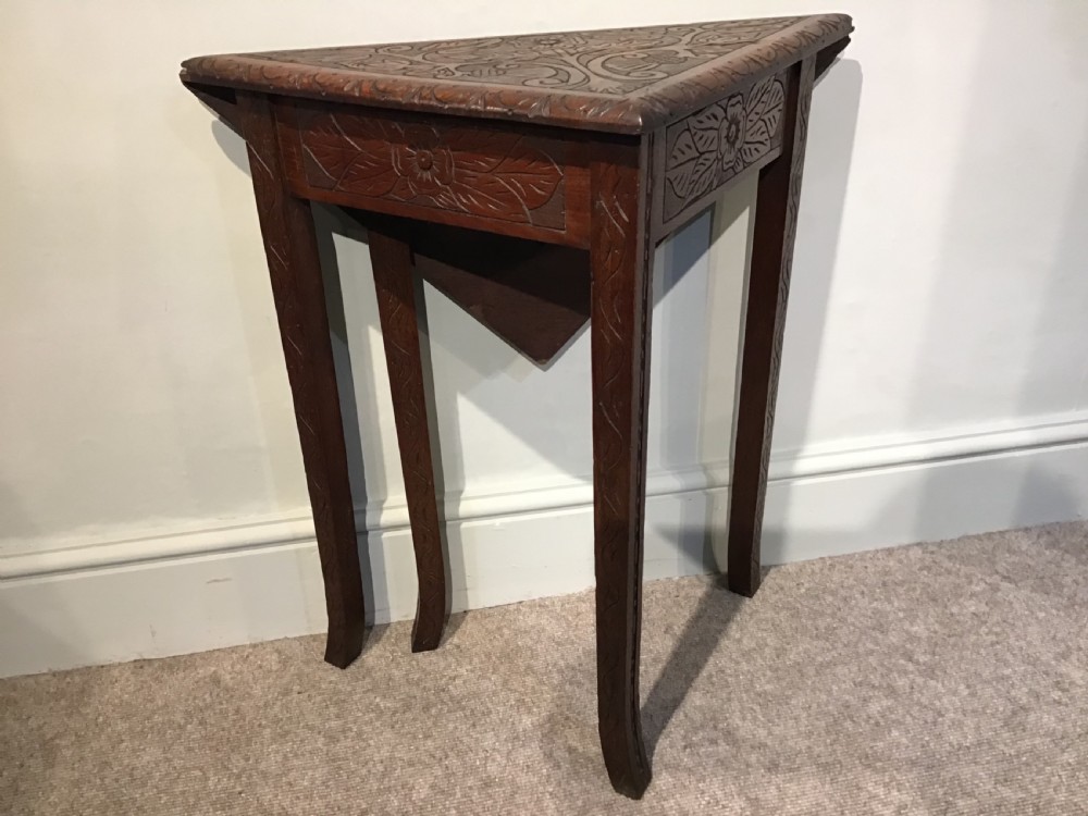 A triangular dark carved wooden corner table featuring intricate relief carvings of leaves and flowers on its top surface and legs. View IV