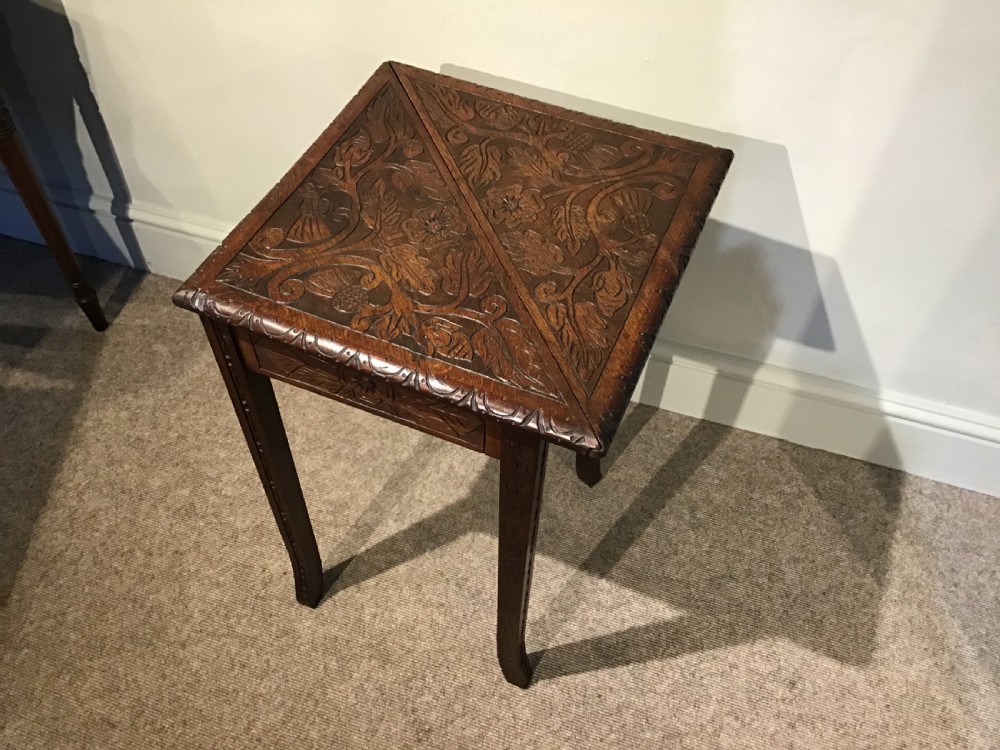 A triangular dark carved wooden corner table featuring intricate relief carvings of leaves and flowers on its top surface and legs. View V