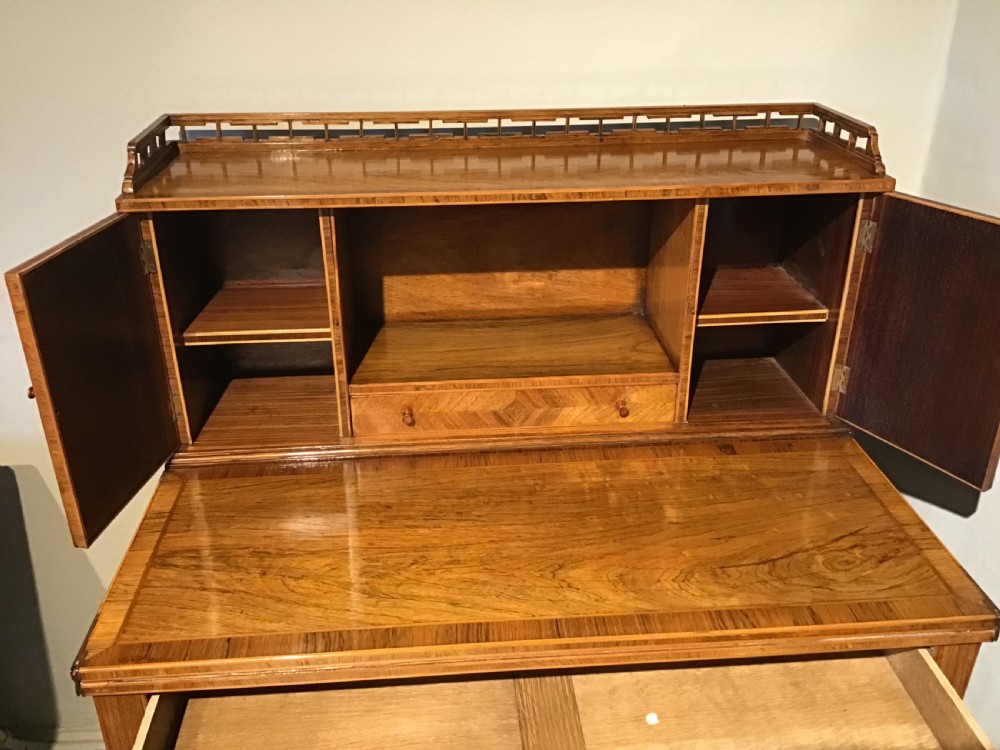 A rosewood bonheur du jour writing desk featuring geometric parquetry veneers, square tapered legs, a frieze drawer, and a raised cabinet top with brass fretwork rail. View IV