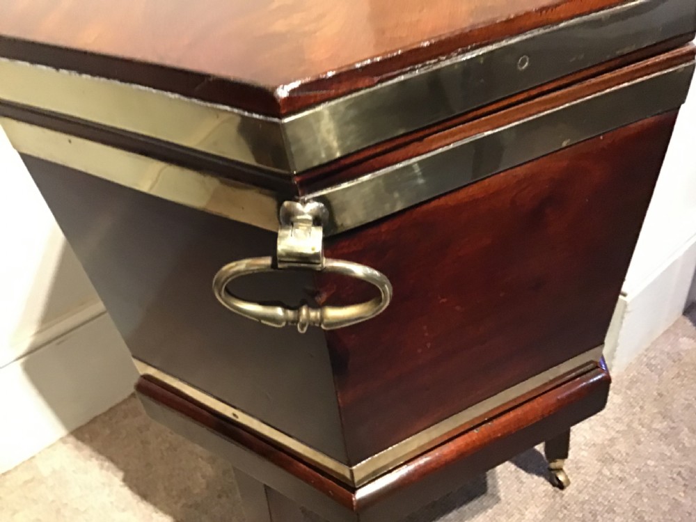 A hexagonal dark mahogany Georgian wine cooler featuring brass binding straps, side handles, and tapered legs on brass castors. View III
